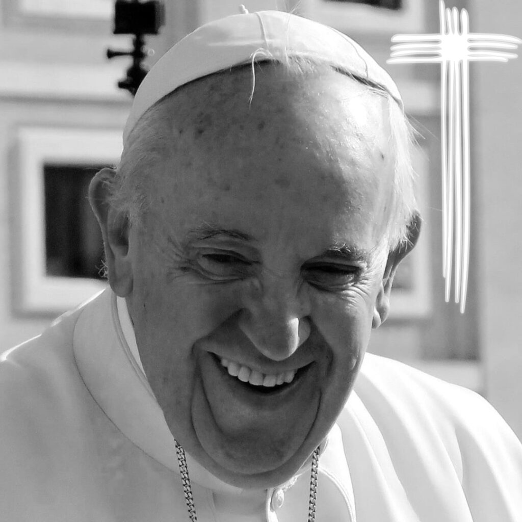 Das Schwarzweiß-Bild zeigt ein Portrait von Papst Franziskus, der in die Kamera lächelt. Oben rechts ist ein Kreuz zu sehen, das aus vier weißen Linien gebildet wird.